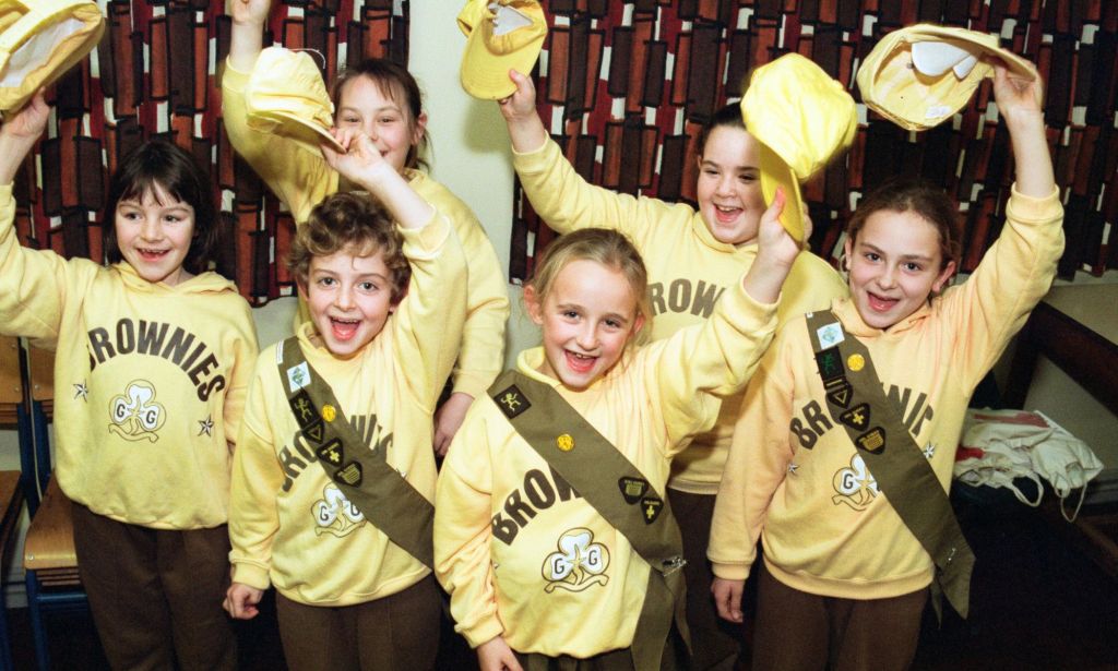 Un groupe d'enfants en uniformes Brownies jaunes et marron levant leurs chapeaux pour une photo.