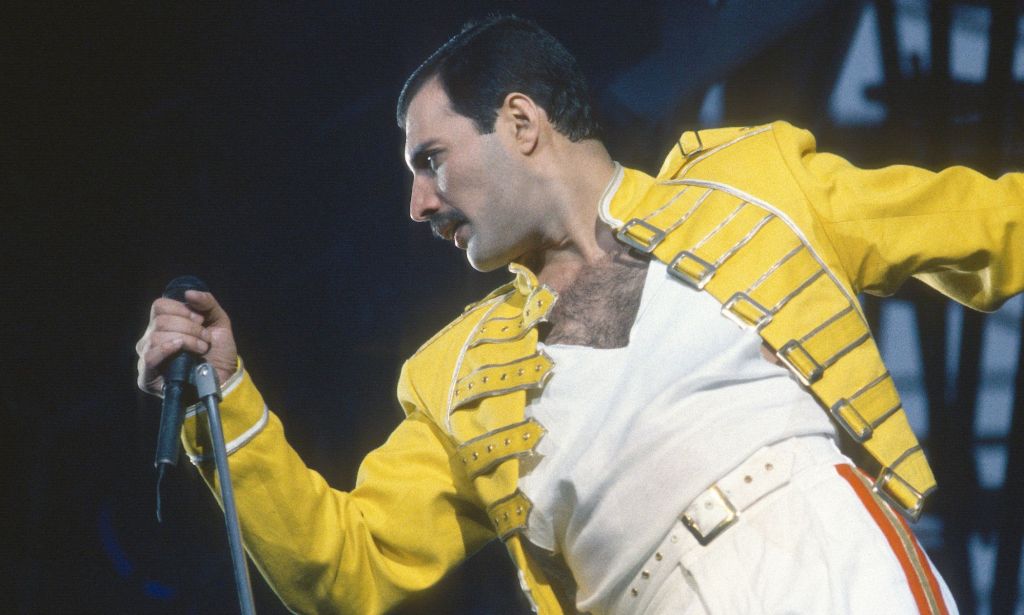 Freddie Mercury se produisant dans sa veste jaune emblématique et son t-shirt blanc.