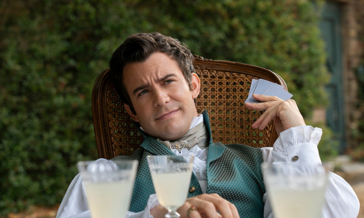 Benedict est-il gay ou bisexuel dans les livres Bridgerton de Julia Quinn ? Benedict Bridgerton sitting in a wooden chair with cards and drinks in front of him