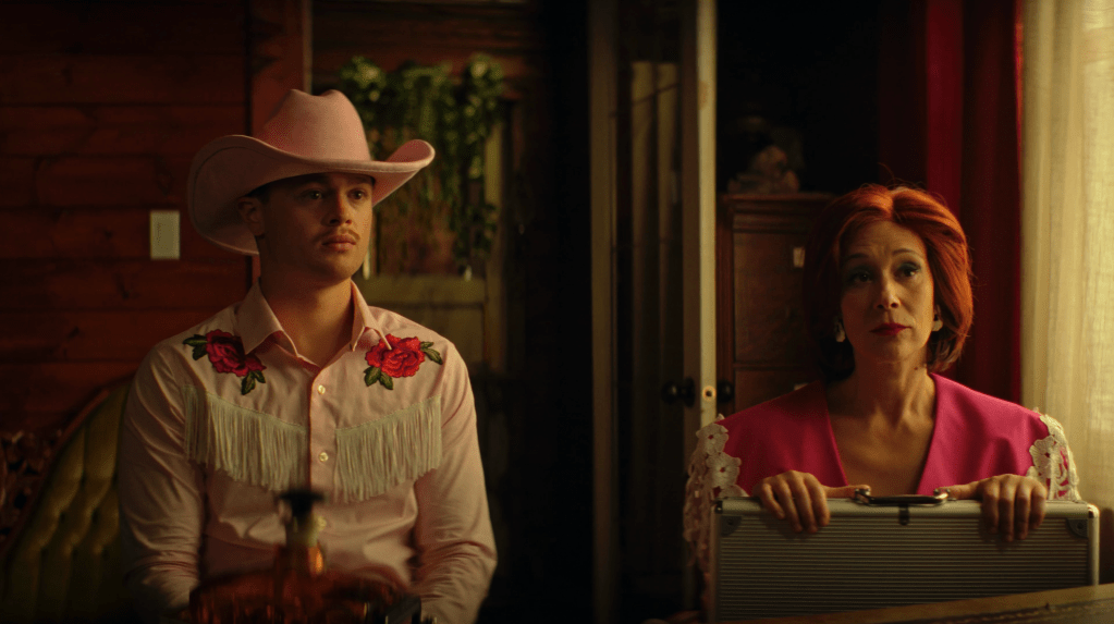 Lunar Sway still : un homme vêtu d'une chemise de cowboy rose et jat était assis à côté d'une femme vêtue d'une veste de pouliche rose, avec une mallette sur ses genoux.