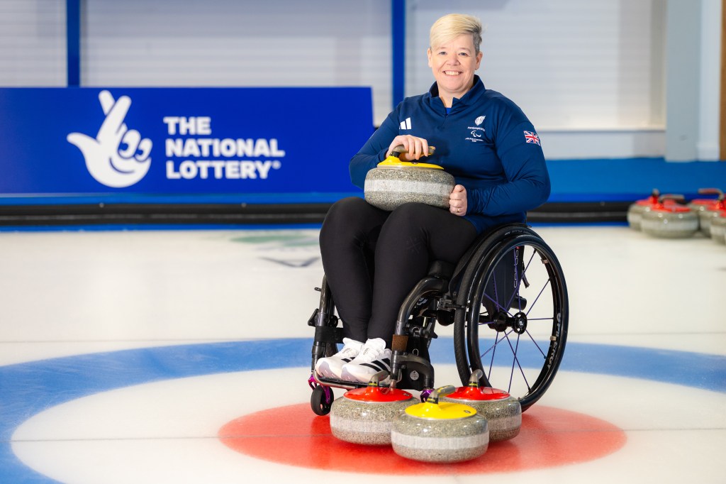 Jo Butterfield dans un fauteuil roulant avec un équipement de curling au sol et sur ses genoux.