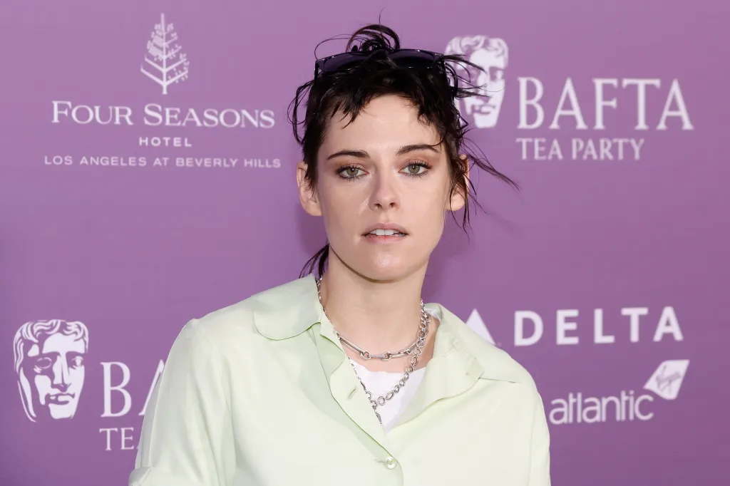 Kristen Stewart dans une chemise jaune pâle et deux colliers en chaîne argentée sur un fond violet BAFTA