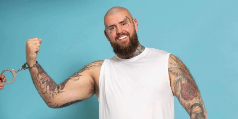 La star d'OnlyFans gay-for-pay enchaînée à la femme au foyer du Sussex 24 heures sur 24 dans Handcuffed de Channel 4 Handcuffed contestant Rob smiling wearing handcuffs while against a blue background.