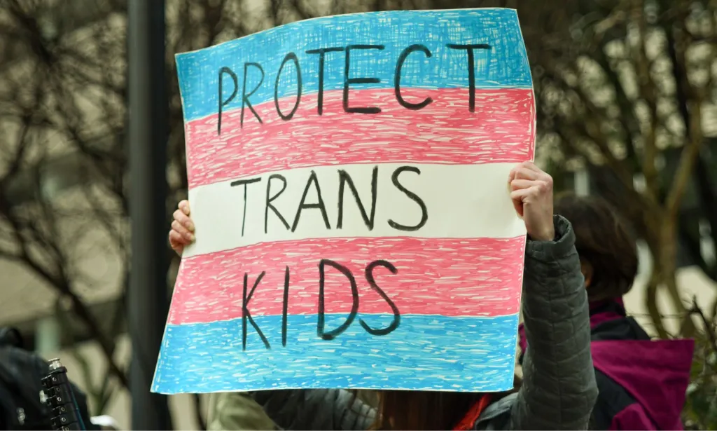Un manifestant brandit une pancarte indiquant « Protégez les enfants trans ».