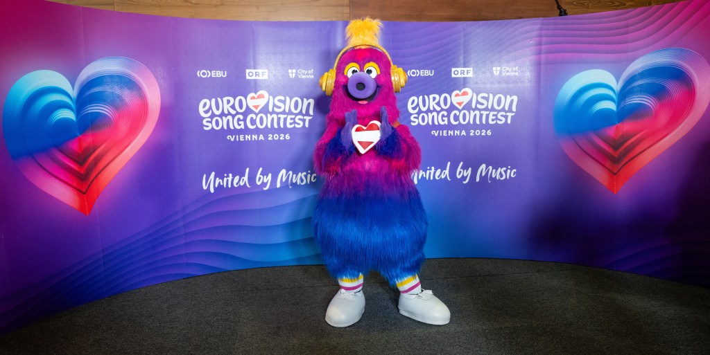 Auri est la mascotte du Concours Eurovision de la chanson 2026. Une créature duveteuse qui a une tête rose qui passe au violet puis aux pattes bleues. Auri porte des baskets et des écouteurs jaunes. Coeur de drapeau de vacances Autriche