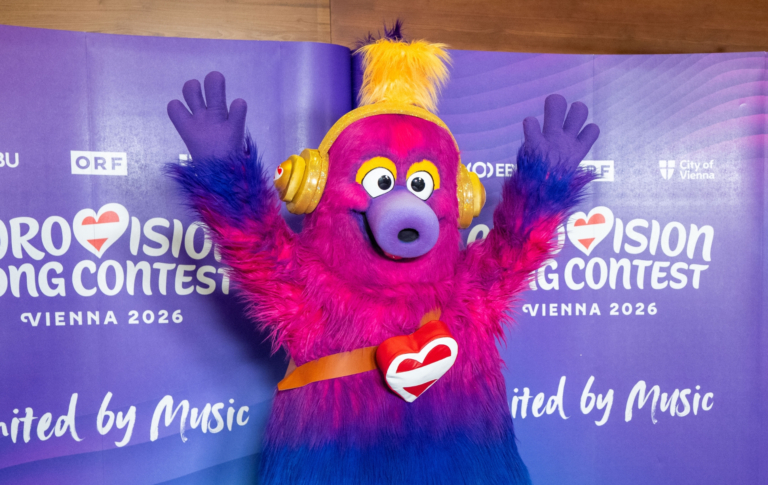 Quel est le thème de l'Eurovision 2026 et qui – ou quoi – est « Auri » ? Auri is the mascot of the 2026 Eurovision Song Contest. A fluffy creature which has a pink head that fades to purple and then blue legs. Auri is wearing trainers and has yellow headphones on. Holiday Austria flag heart