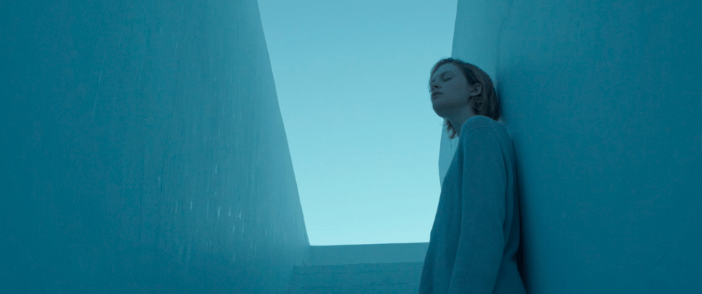 Emma Laird dans le rôle de Lola dans Satisfaction. Elle monte des marches blanc pâle vers le ciel bleu, l'image est d'un ton bleu délavé.