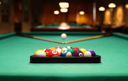 Plastic triangle rack with billiard balls and cues on green table indoors