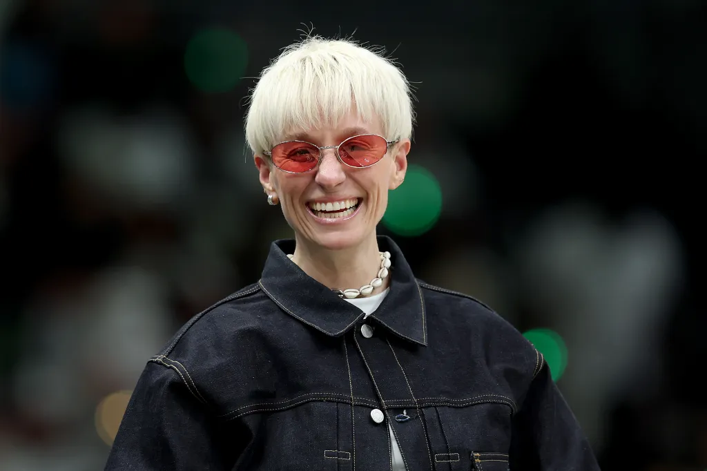 Photo de Megan Rapinoe, souriante avec des lunettes roses et une veste en jean foncé