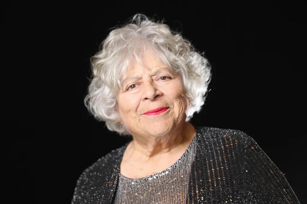 Miriam Margolyes pose lors d'une séance photo avant la 98e cérémonie des nominés aux Oscars. Elle porte un haut gris à paillettes et un cardigan gris foncé à paillettes.