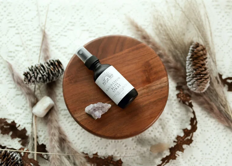 Une bouteille de spray de magnésium Piece of Mynd's Sacred Bliss sur une table avec des pommes de pin et des cristaux