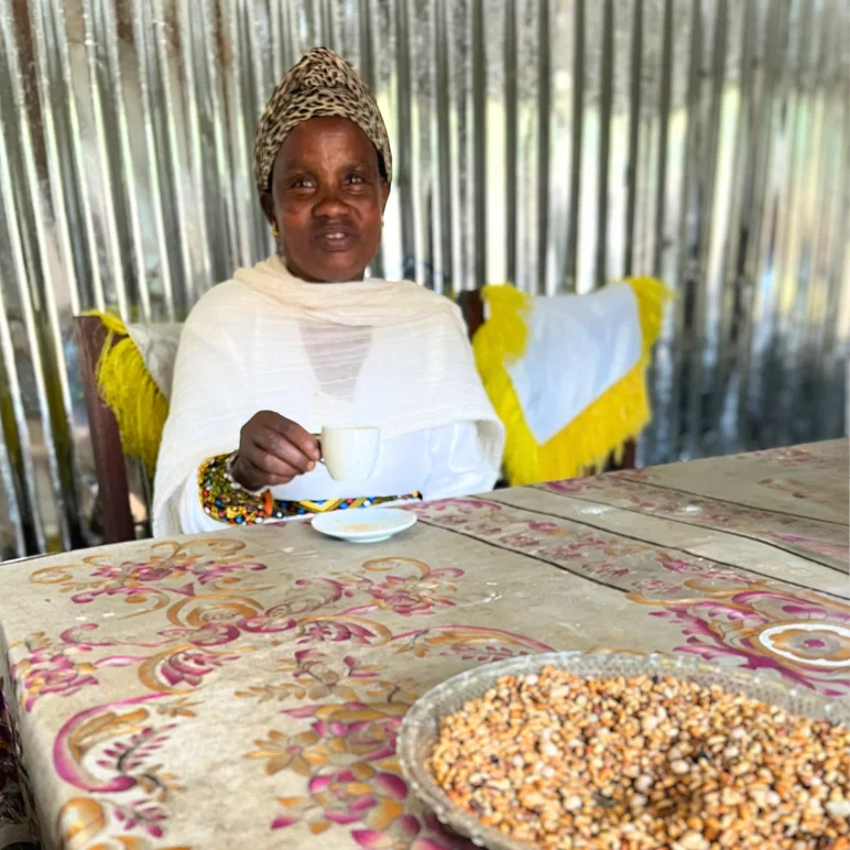 Une femme éthiopienne boit du café à une table avec des grains de café crus en train d'essayer devant elle