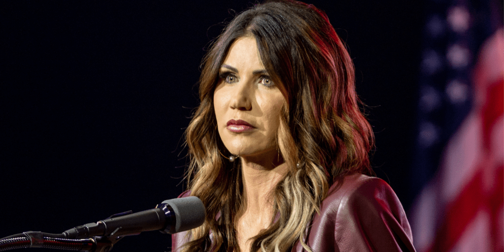 Une photo montre la gouverneure républicaine du Dakota du Sud, Kristi Noem, debout derrière un microphone avec le drapeau américain en arrière-plan.