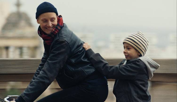 Love Me Tender still : une femme faisant du vélo avec un enfant à l'arrière du vélo