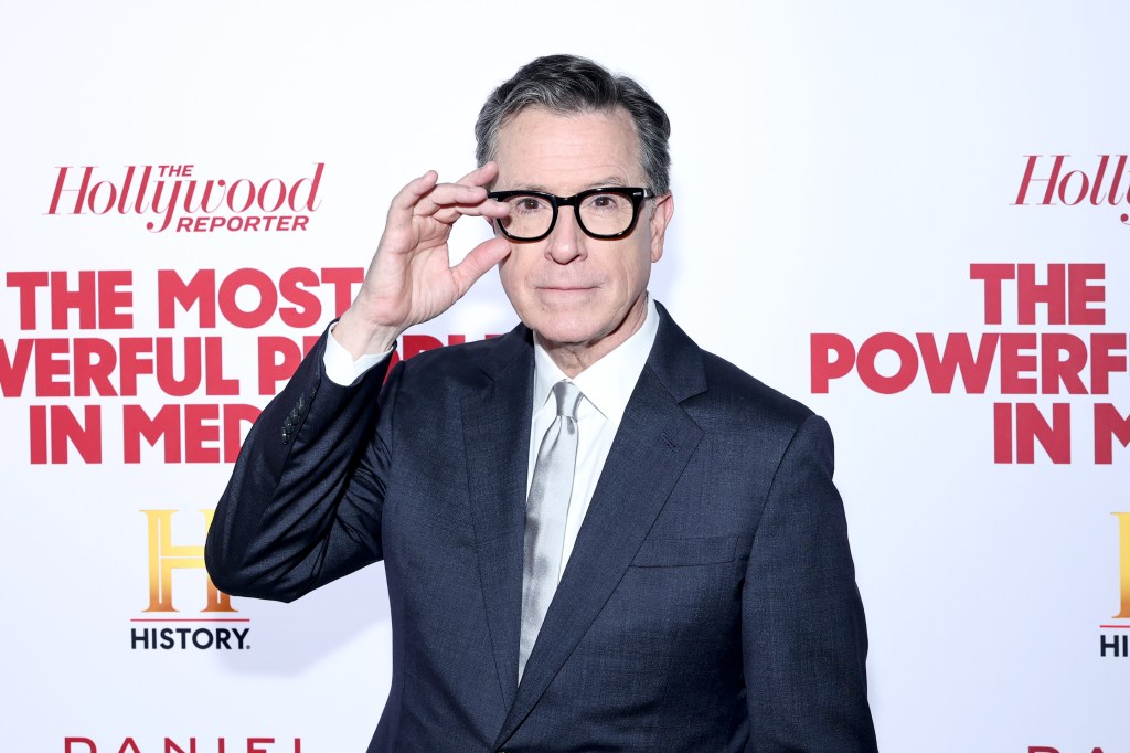 Stephen Colbert en costume, tenant ses lunettes