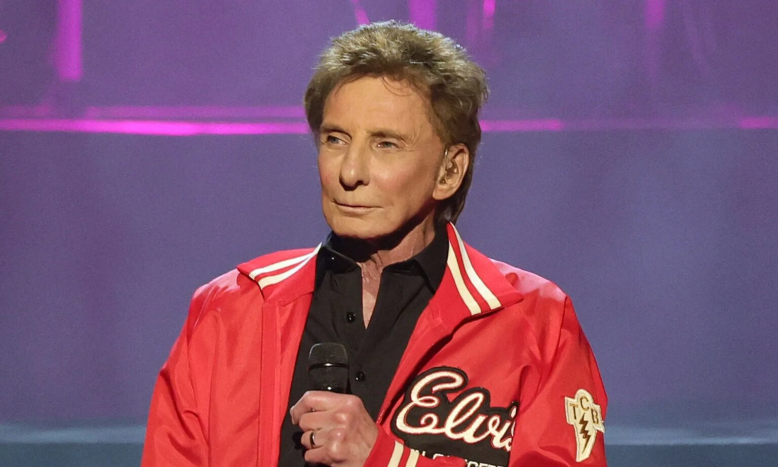 Barry Manilow dit que faire son coming-out plus tôt « aurait tué » sa carrière Singer Barry Manilow wears a black shirt and red jacket as he holds a microphone in front of his chest