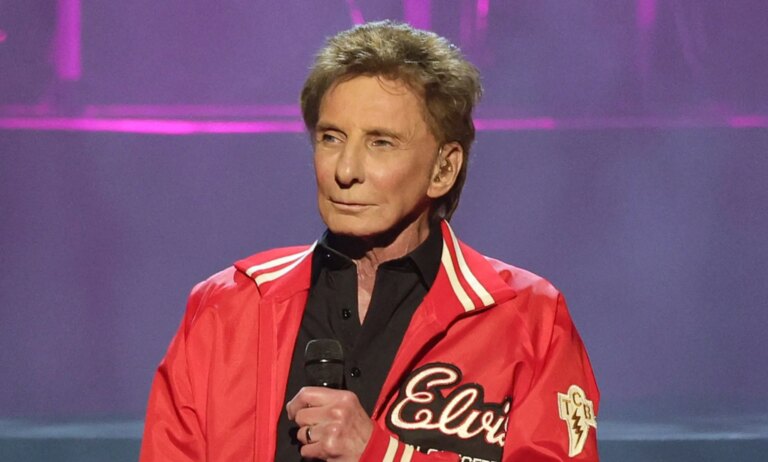 Barry Manilow dit que faire son coming-out plus tôt « aurait tué » sa carrière Singer Barry Manilow wears a black shirt and red jacket as he holds a microphone in front of his chest
