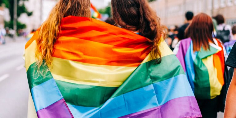 Signification de l'acronyme LGBTQ+, y compris le plus et son histoire Two women wearing an LGBTQ+ Pride flag