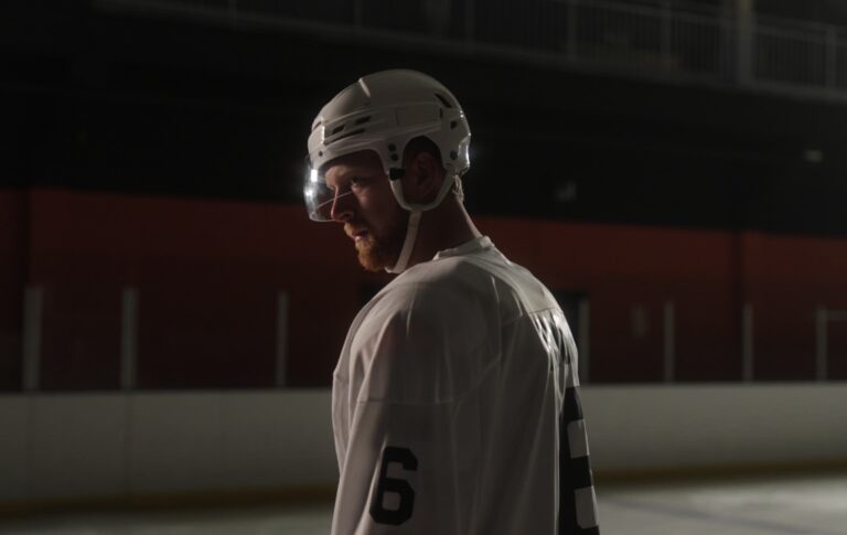Le joueur de hockey sur glace gay Luke Prokop parle de sa représentation du sport et de l'impact révolutionnaire de Heated Rivalry Luke Prokop in ice hockey gear in a dim rink