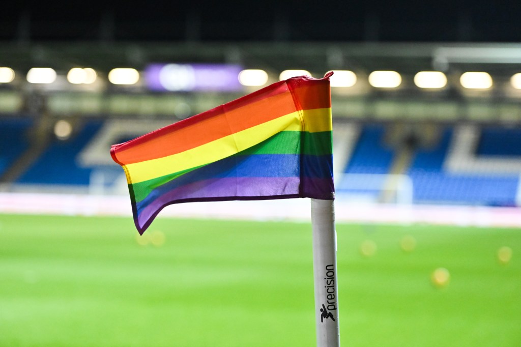 Drapeau arc-en-ciel planté sur un terrain de football.