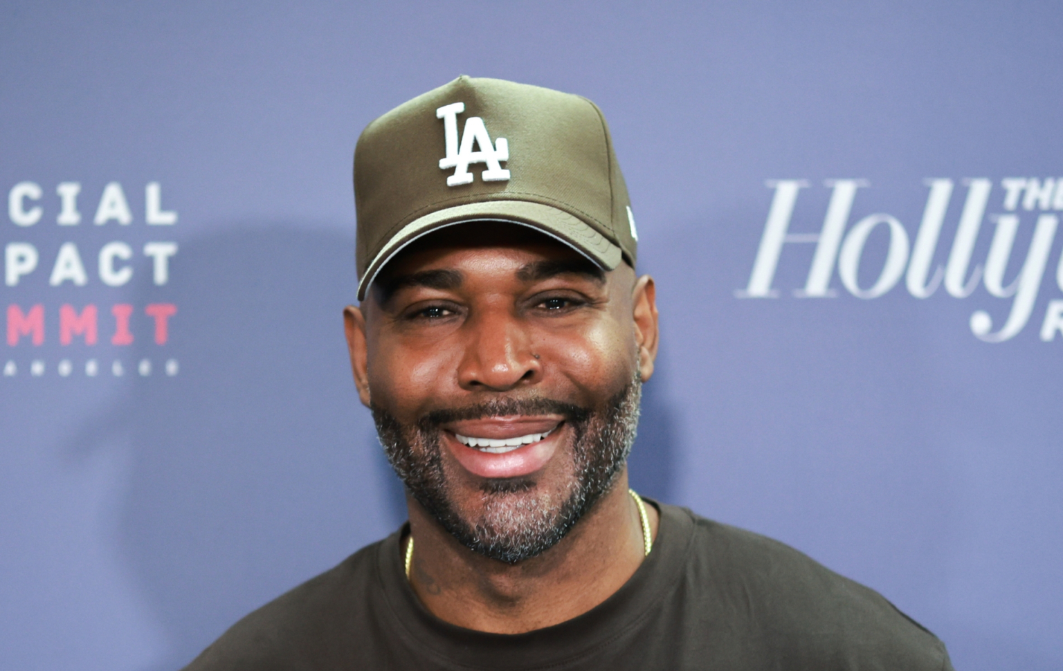 Karamo Brown affirme que le directeur de Queer Eye a menacé de le licencier lors de la première saison Karamo Brown smiling on a red carpet against a blue background. He