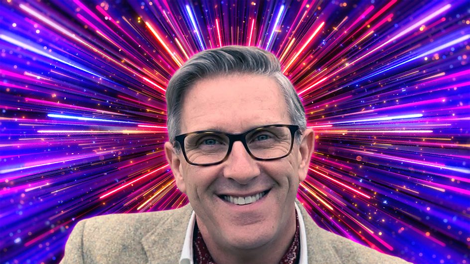 Graeme Hall dans un costume crème avec des feux d'artifice strictement colorés derrière lui