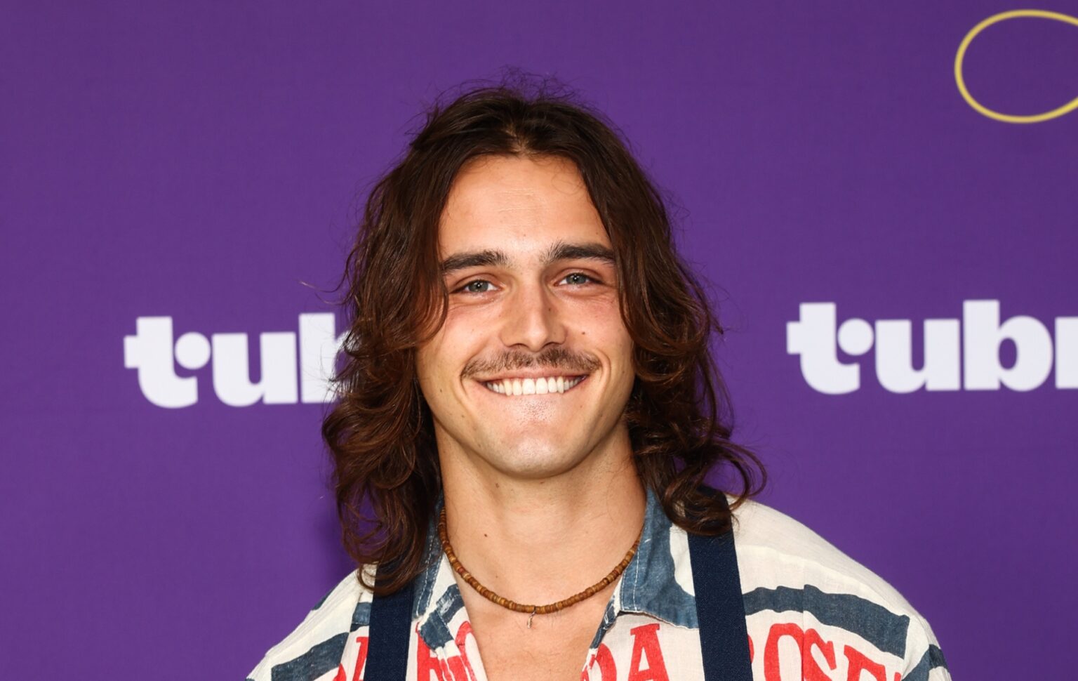Rencontrez Charlie Gillespie, la star de Heated Rivalry saison 2, Troy Barrett Charlie Gillespie smiling against a purple background