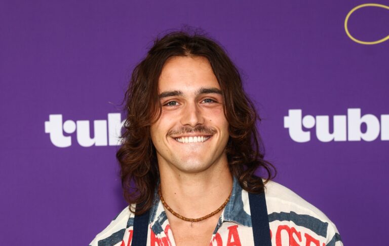 Rencontrez Charlie Gillespie, la star de Heated Rivalry saison 2, Troy Barrett Charlie Gillespie smiling against a purple background