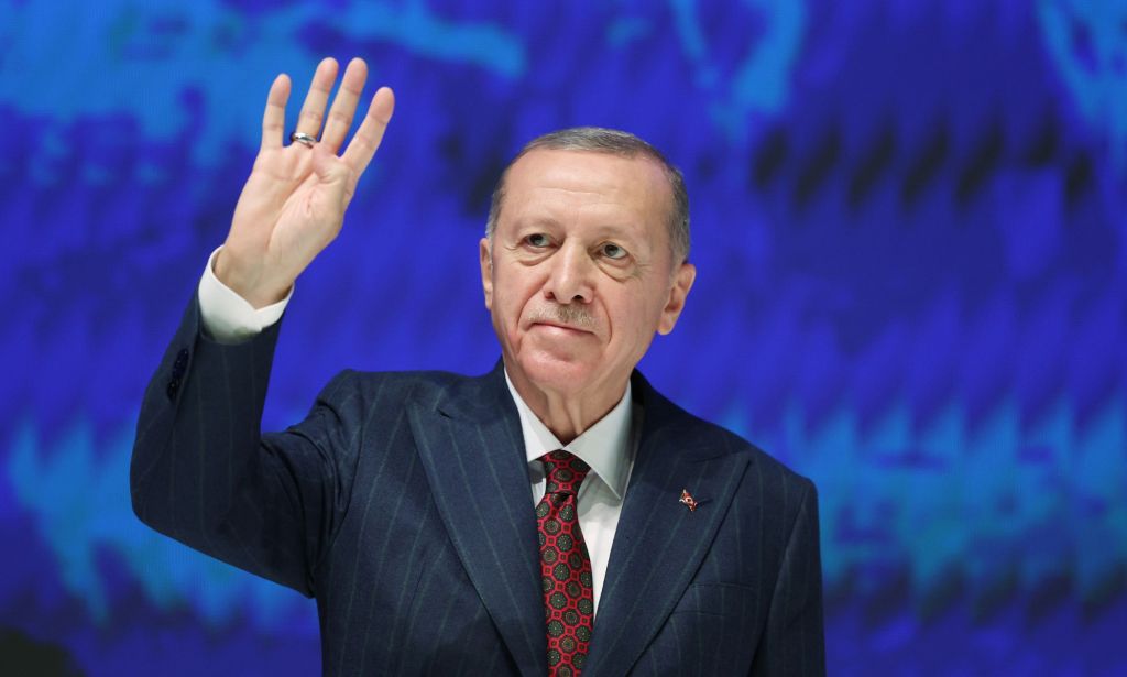 Le président turc Recep Tayyip Erdoğan, qui a l'habitude de tenir des propos anti-LGBTQ+, porte un costume et une cravate alors qu'il lève une main lors d'une conférence politique