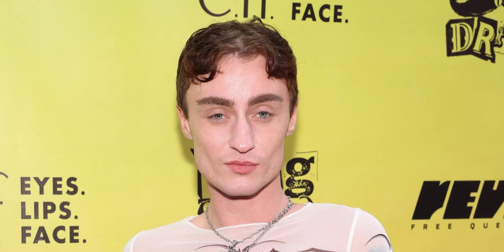 L'artiste de drag Gottmik se tient devant un fond jaune lors d'un événement.