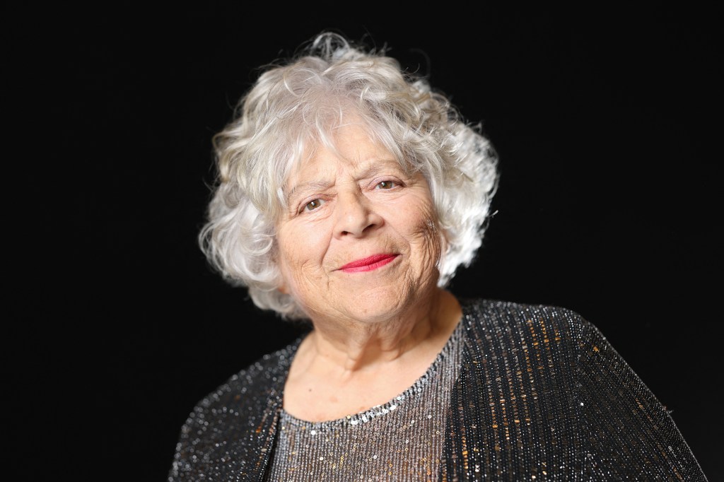 Miriam Margolyes pose lors d'une séance photo avant la 98e cérémonie des nominés aux Oscars. Elle porte un haut gris à paillettes et un cardigan gris foncé à paillettes.