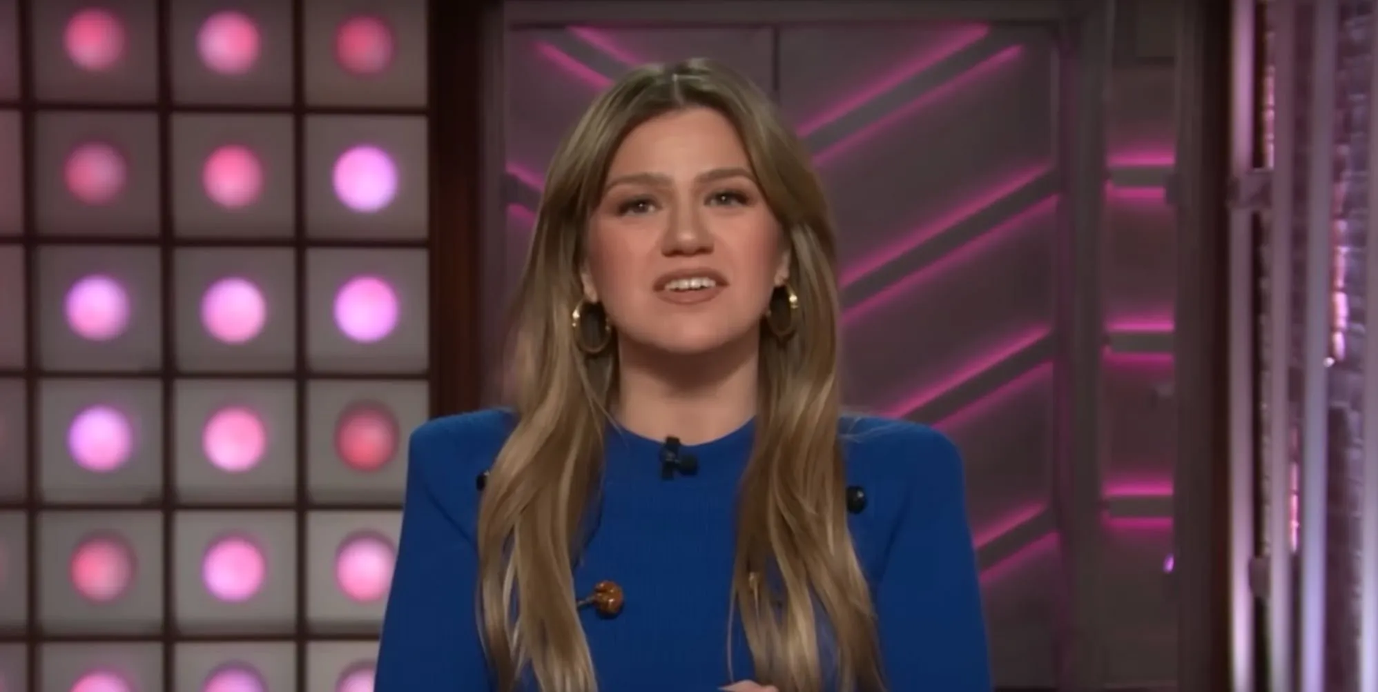 Kelly Clarkson s'adressant à la caméra lors de son talk-show, vêtue d'un pull bleu.