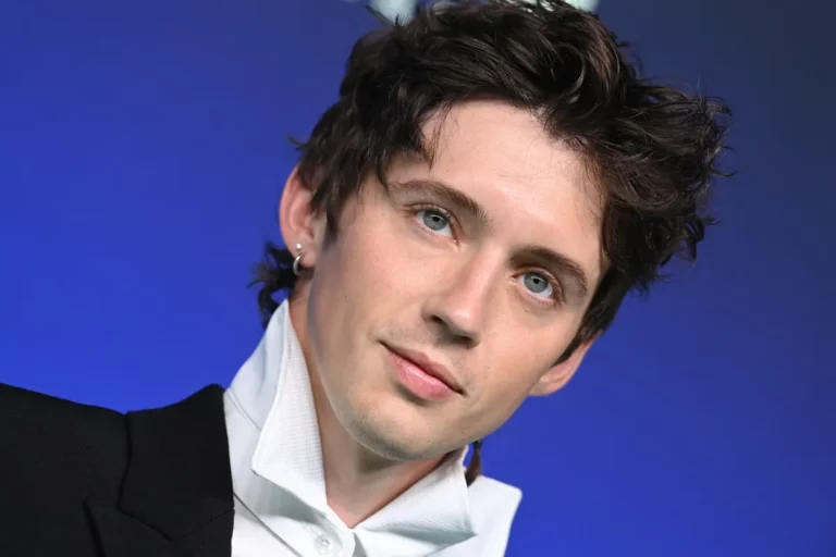 Troye Sivan sur la masculinité, les intimidateurs et le professeur qui l'a laissé chanter au lieu de nager Troye Sivan at the 2026 MTV Video Music Awards in Los Angeles, looking toward the camera in a black jacket and white collar